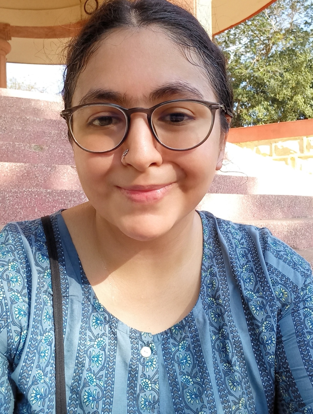 Portrait of the author Kunjana Parashar. Kunjana is wearing brown glasses and a blue blouse with a flowery pattern.