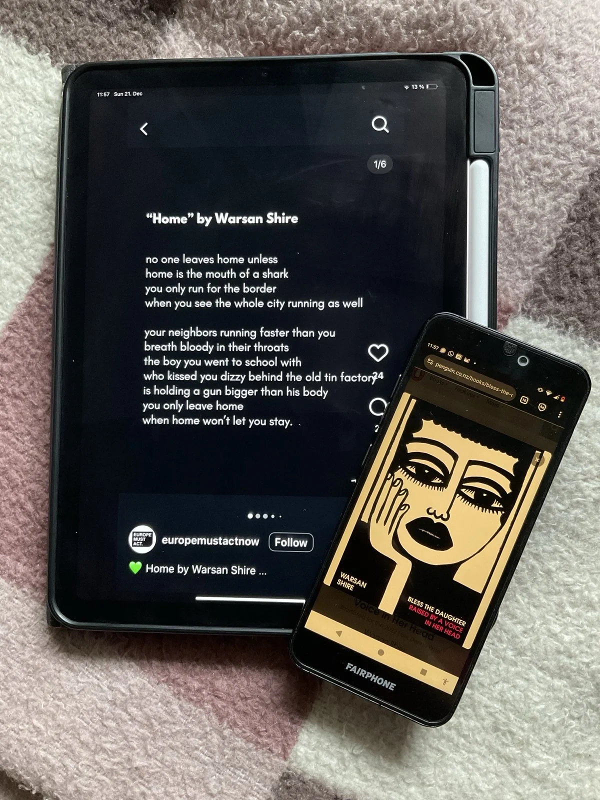 A tablet with an open Instagram post by europemustactnow of two verses of the poem "Home" by Warsan Shire (white font on black background). Lying on the lower right corner of the ipad is a phone with a picture of the book cover of "Bless the Daughter," the poetry collection by Warsan Shire, opened on it. Phone and tablet are lying on a checkered white-brown-rose blanket.